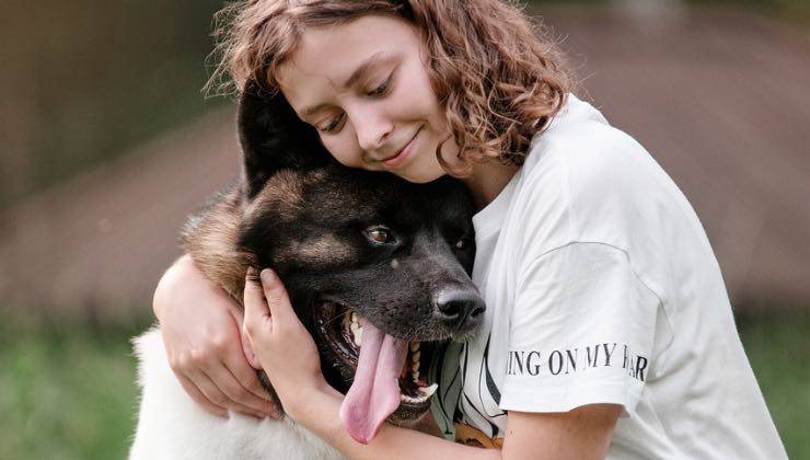 Ragazza abbraccia un quattro zampe dal muso nero 